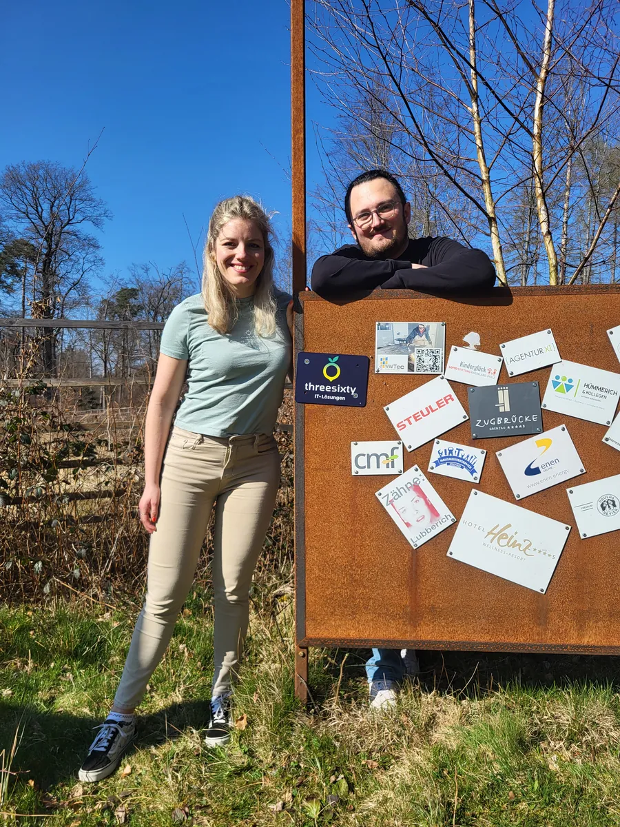 Carina Jockschat und Johannes Lewin von threesixty an der Patentafel der Westerwald-Kinder im Wald, mit dem frisch angebrachten threesixty-Schild